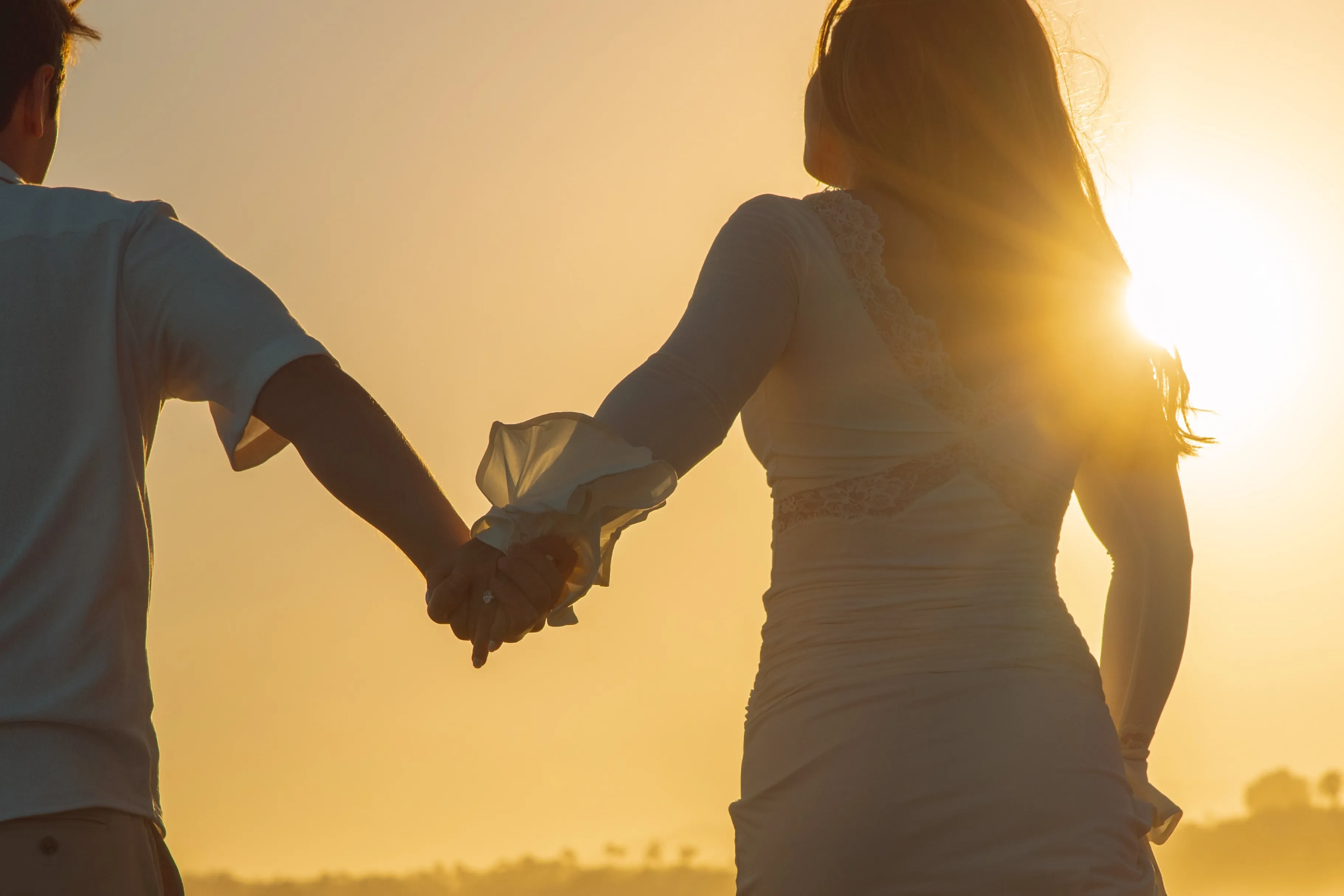 Couple holding hands against a sunset silhouette